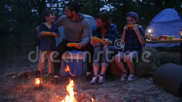 在大自然的火焰附近吃晚餐家人用盐吃玉米旅行野营妈妈爸爸和儿子吃新鲜的黄色玉米视频的预览图