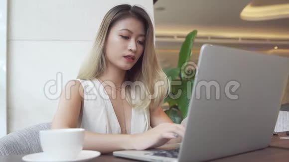 亚洲女商人用手提电脑微笑着喝咖啡视频的预览图