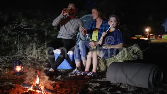 美国家庭在林地的旅行营父母喝啤酒孩子在带帐篷的旅途中在篝火旁吃zephyr视频的预览图