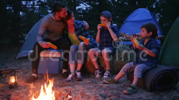 在大自然的火焰附近用餐一家人享用含盐的玉米户外野餐野营爸爸妈妈和儿子吃视频的预览图