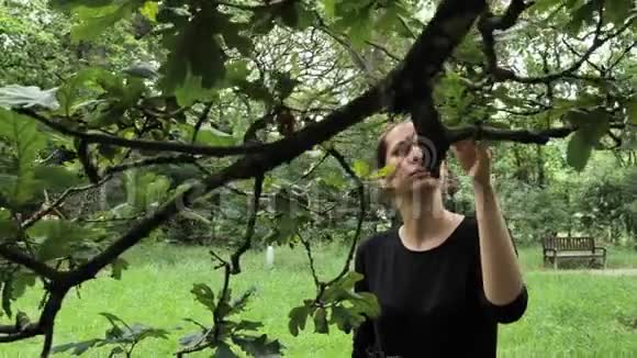 4K漂亮的女孩穿着黑色手工制作的裙子走在美丽的绿色明亮的花园里抚摸着树叶穿着视频的预览图