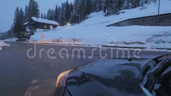 黑暗的汽车头灯在道路上沿着白雪覆盖的树木和山丘移动视频的预览图