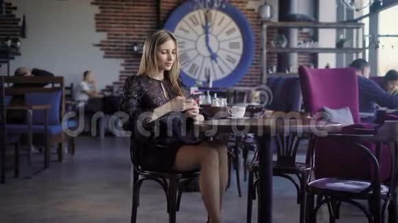 女商人穿着黑色连衣裙享受午餐休息坐在咖啡馆里背景是人们使用现代视频的预览图