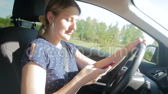 年轻女司机开车上路时使用智能手机的慢速镜头视频的预览图