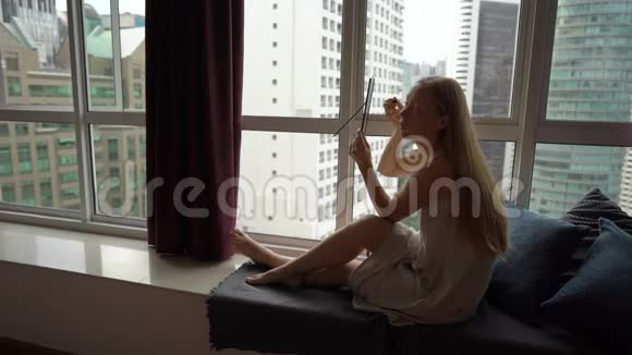 一位年轻女子在市中心的一扇全景窗旁化妆的超级慢镜头视频的预览图