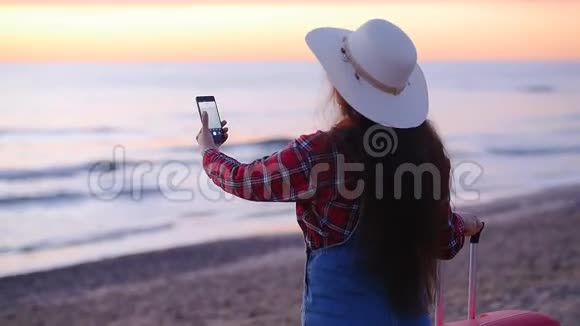 年轻的女游客在海边为日落或黎明拍照视频的预览图