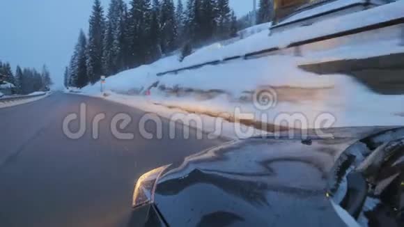 黑色的汽车与前灯在道路上移动沿雪覆盖的树木和山丘视频的预览图