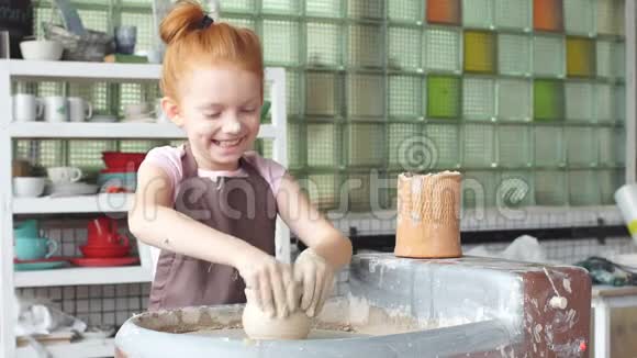 快乐的孩子正把一个陶土花瓶压在车轮上孩子正慢慢地在陶轮上工作然后把一个花瓶塑成一个金色的小花瓶视频的预览图