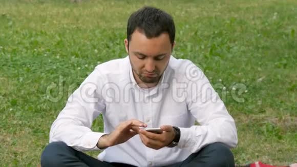 英俊的成年男子在阳光明媚的傍晚在公园户外用手机发送短信视频的预览图
