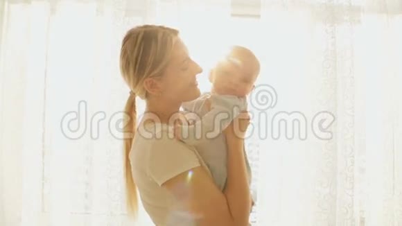 幸福的年轻妈妈抱着她可爱的微笑小男孩在窗前的画像视频的预览图