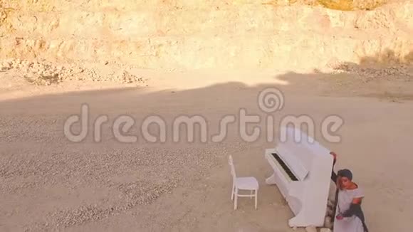 梦中的女孩在黄色的山脉和石头中靠近白色的钢琴不寻常的情节空中观景视频的预览图