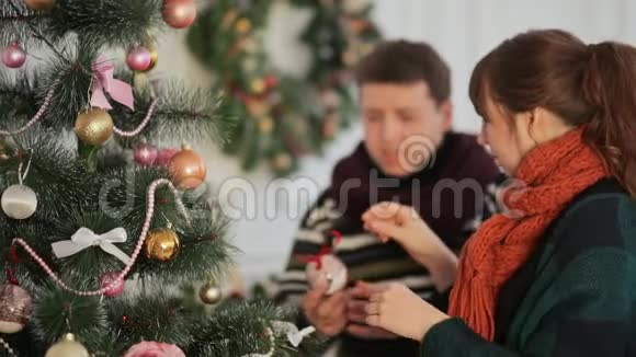 美丽的年轻夫妇爱装饰圣诞树安排圣诞灯和乐趣视频的预览图