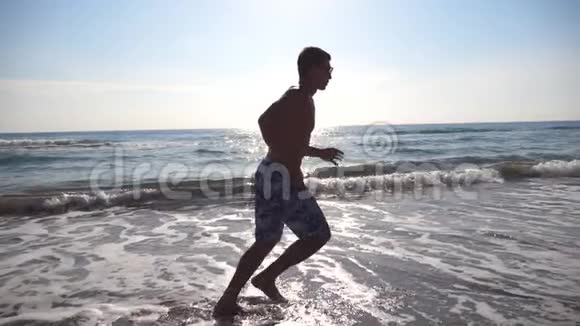 早上在海边跑步的运动青年在阳光明媚的日子里运动员沿着海岸慢跑男运动员视频的预览图