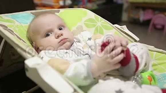 可爱的婴儿躺在儿童的摇椅试图举起他的袜子视频的预览图