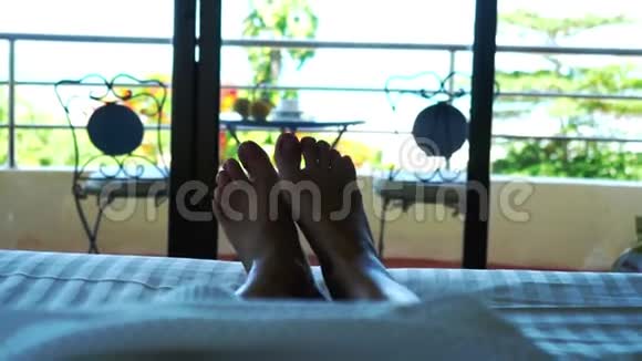 女人躺在酒店的床上挥舞着她的脚对着热带海景3840x2160视频的预览图