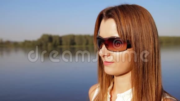 肖像女子戴墨镜站在江岸河岸上微笑的女人的肖像近点视频的预览图