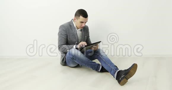 4一个带耳机的年轻人坐在办公室的地板上在平板电脑上工作视频的预览图