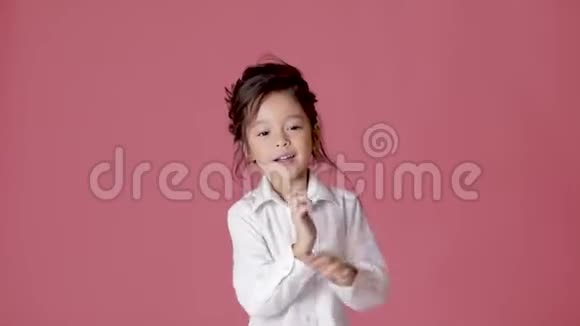 穿着白色衬衫在粉红色背景上跳舞的小女孩视频的预览图