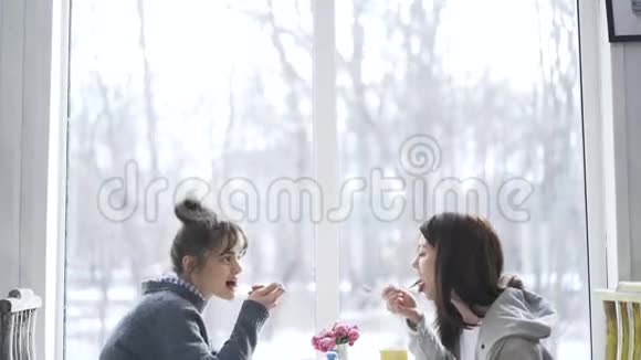 两个年轻的大学生女孩在咖啡馆里吃饭说话倾斜下来视频的预览图