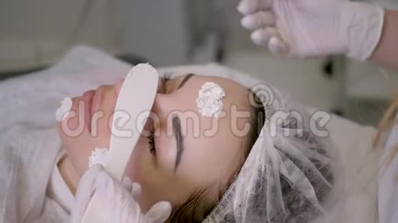 戴橡胶手套的美容医生在脸上涂霜视频的预览图