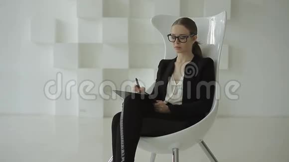 年轻的商务女士坐在未来的白色办公室里在笔记本上写一些东西视频的预览图