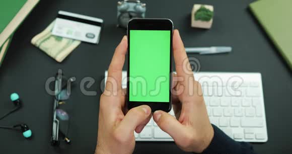 男人拿着一个绿色屏幕的黑色智能手机在工作桌上敲了敲它的东西视频的预览图