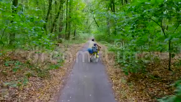 一个人走着走上马路在森林里和一个孩子开着自行车孩子坐在一张特殊的椅子上夏季视频的预览图