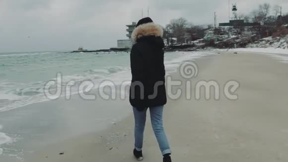 在寒冷的冬天年轻漂亮的女人在海滩上走来走去慢动作视频的预览图