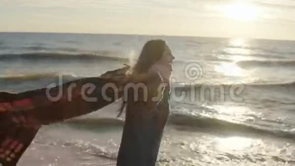 年轻快乐的女人在日落时在海滩上散步美丽的雌鸟用伸展的臂膀撑着格子花在海边视频的预览图