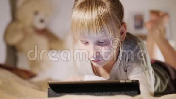小女孩躺在卧室的床上用平板电脑视频的预览图