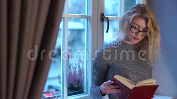 这位戴着眼镜在窗户附近看书的聪明漂亮女孩的半身像她在寻找视频的预览图