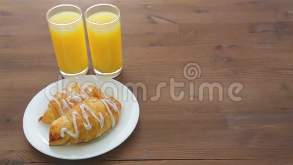 木桌上摆着两杯橙汁和一盘羊角面包视频的预览图