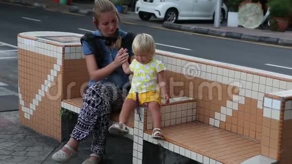 金发女郎与母亲坐在靠近马路的长凳上视频的预览图