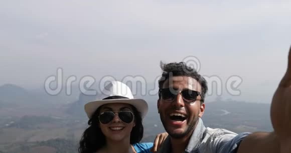 喜笑颜开的情侣在山顶上自拍照美丽的景观POV混合种族男女游客视频的预览图