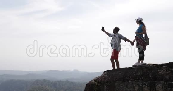游客情侣站在山顶在手机智能手机上制作视频景观青年男女旅行者手持视频的预览图