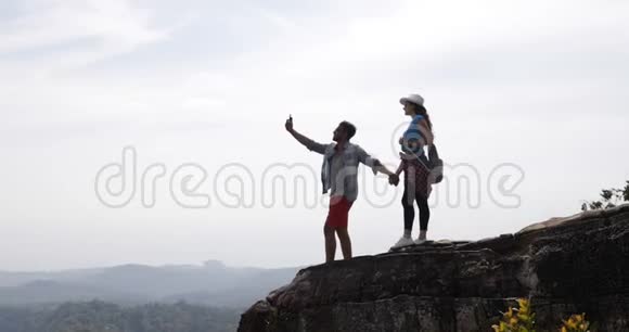 游客情侣站在山顶在手机智能手机上制作视频景观青年男女旅行者手持视频的预览图