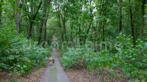一个人走着走上马路在森林里和一个孩子开着自行车孩子坐在一张特殊的椅子上夏季视频的预览图