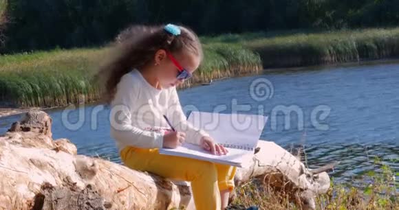 碰巧小女孩坐在河边在石碑上画画视频的预览图
