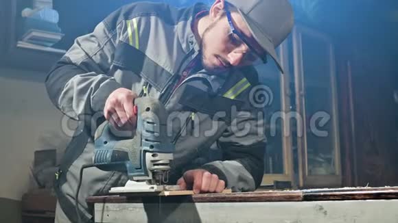 一个留着灰色工作服和护目镜的年轻人一个木匠在家里做电锯视频的预览图