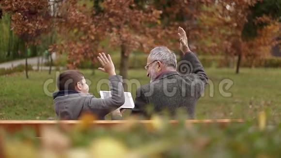 爷爷和孙子一起在公园里度过时光他们坐在长凳上用平板电脑视频的预览图