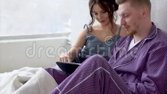 两个穿着睡衣坐在床上看着平板电脑上的新赛季视频的预览图