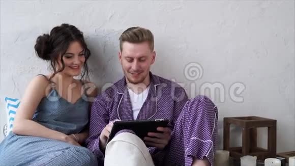 一对相爱的夫妇穿着睡衣在平板电脑上选择一家酒店度假视频的预览图