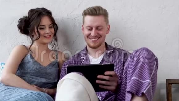 年轻夫妇躺在床上看平板电脑上的视频视频的预览图