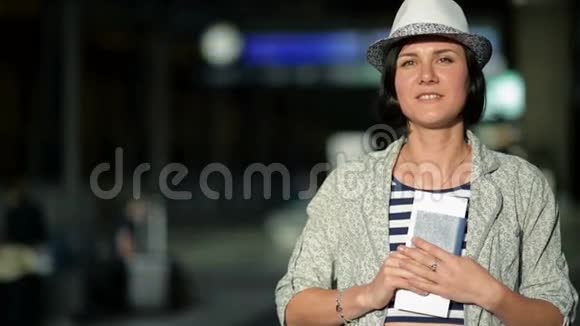 短发夏帽带条纹的年轻不伦黛的肖像在镜头前展示她的护照和机票视频的预览图