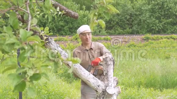 一个人在他家附近砍了一棵链锯树背景中的绿树移除干燥的树枝视频的预览图
