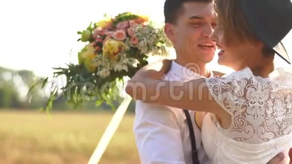 微笑的新婚夫妇和拥抱在阳光明媚的田野里的侧面肖像新娘手里拿着五颜六色的视频的预览图