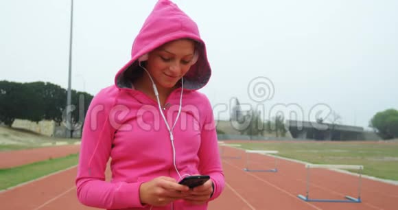女子运动员在4k体育场地听手机音乐视频的预览图