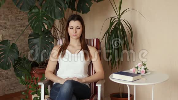 一个年轻漂亮的女孩从桌子上拿起一本书开始阅读坐在椅子上看书的女人视频的预览图