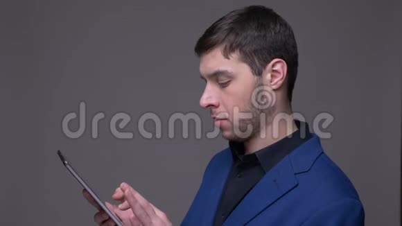 年轻英俊的白种人用平板电脑在镜头前拍摄特写镜头背景是灰色的视频的预览图