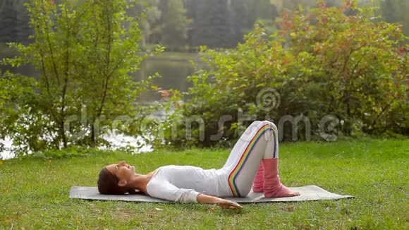 年轻女子在河岸躺在瑜伽垫上做肩飞运动视频的预览图